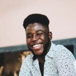 Happy African American man smiling while holding a phone and enjoying coffee indoors.